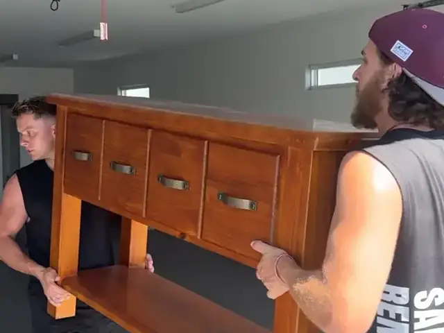 Two Safepack removalists carrying a timber cabinet through a garage