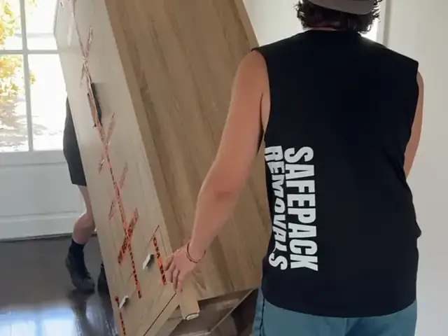 Safepack removalist moving a large timber cabinet on a trolley inside a home