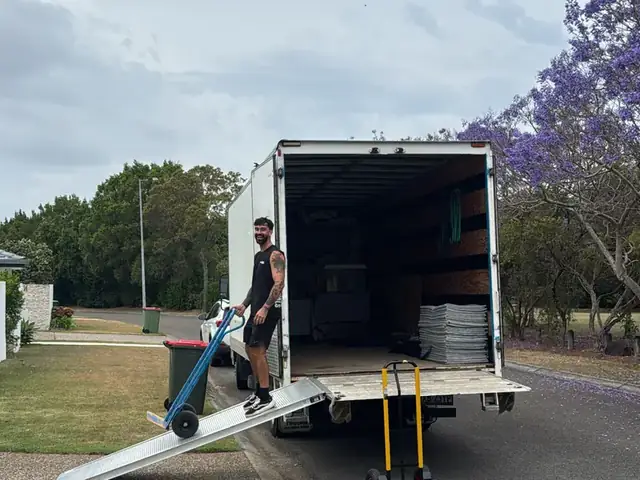 Safepack removalist wheeling furniture on a trolley up the truck ramp under a jacaranda tree